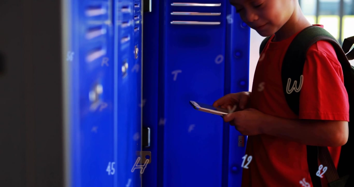 Boy standing by blue lockers, tapping phone and using school app to open locker now