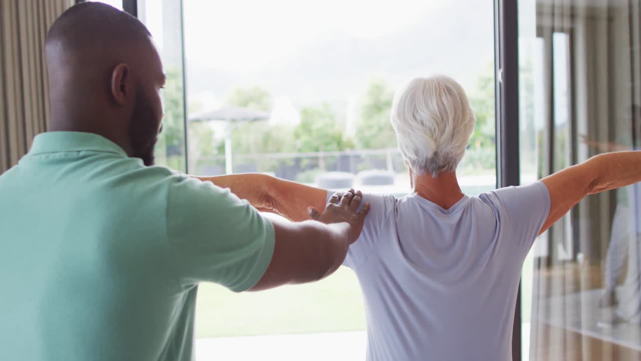 Video of back view of african american male physiotherapist exercising with caucasian senior woman