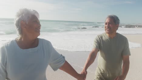 feliz pareja de adultos mayores hispanos caminando por la playa al atardecer