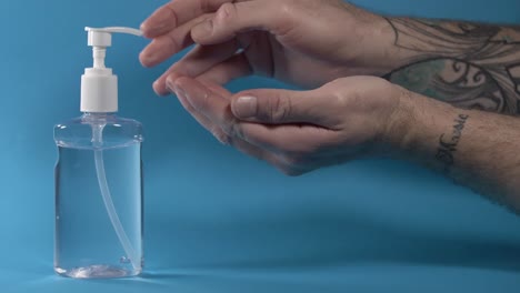 Slow-Motion-Of-Spraying-And-Rubbing-Liquid-Sanitizer-On-Hands-In-Blue-Background---close-up