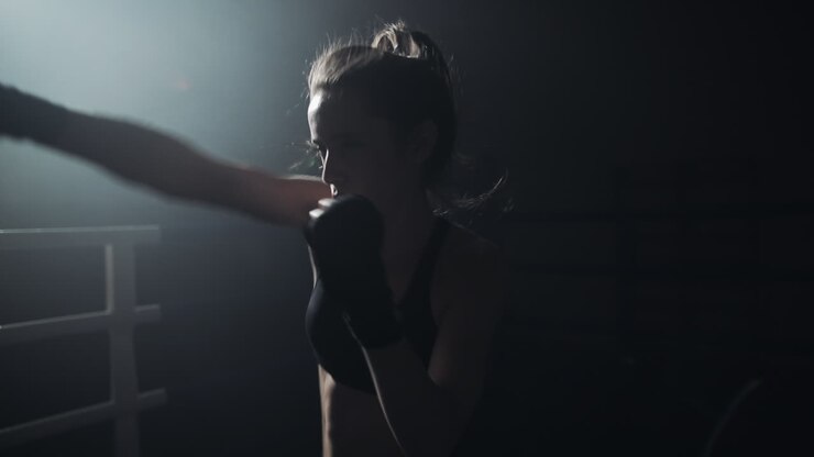 Pugile donna che si allena in un ring buio con un riflettore