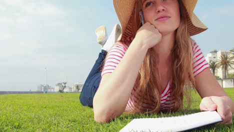 hermosa estudiante joven acostada en el césped estudiando