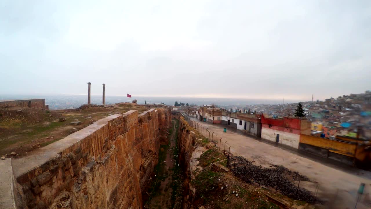 la zanja del castillo de urfa divide las ruinas y los barrios marginales lejos dos columnas los pájaros vuelan nieve y lluvia panorama