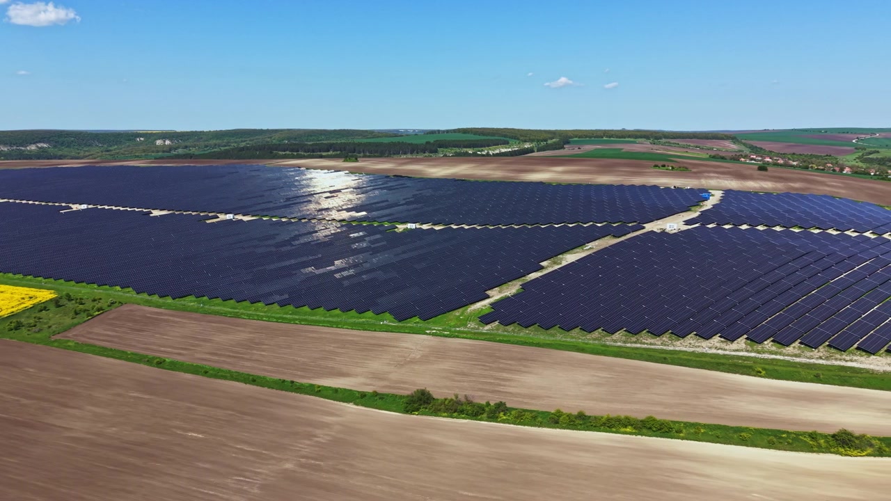 Solpaneler dækker et stort område på en mark om dagen med klar blå himmel og fjern grøn beplantning i baggrunden.