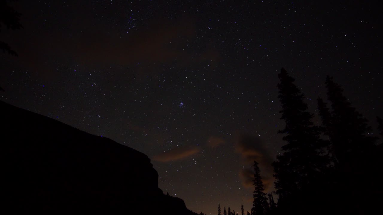 Time lapse of a Starry sky rolling by silhouetted mountains and trees in the Ghost public land use zone. Alberta Canada