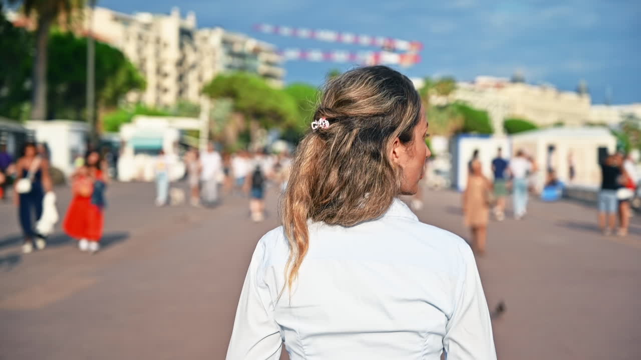 Rear view of a walking woman, walking people on an embankment street in Cannes, France. Slow motion