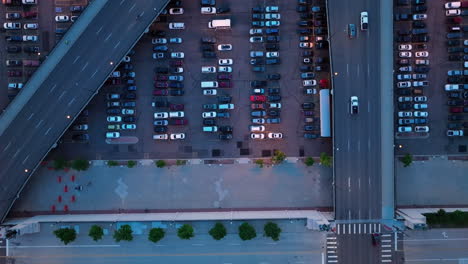 Top-down-aerial-over-full-parking-lots-under-highway-overpass-with-light-traffic