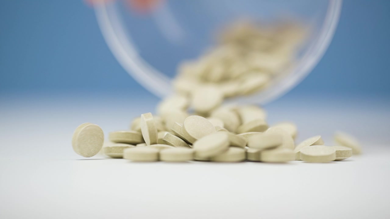 Compresse beige chiaro cadono delicatamente su una superficie bianca immacolata al rallentatore in 4K. I toni tenui e le texture lisce creano un'estetica minimalista e serena, evidenziando il movimento dinamico