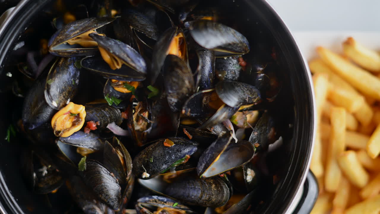 Mejillones cocinados servidos en una olla con hierbas y salsa, acompañados de patatas fritas doradas.