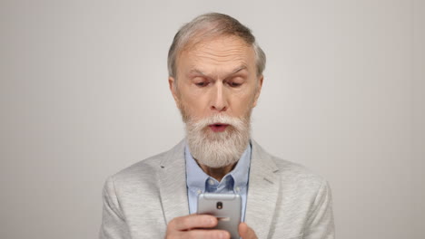 Senior-man-scrolling-on-cellphone-in-studio.-Surprised-guy-using-phone-indoors.