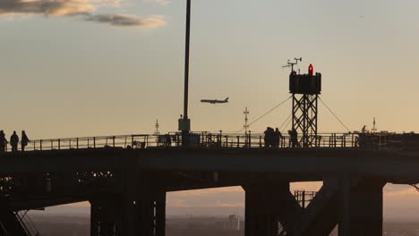 tourist standing on top of the harbour bridge in sydney while an airplane approach the airport