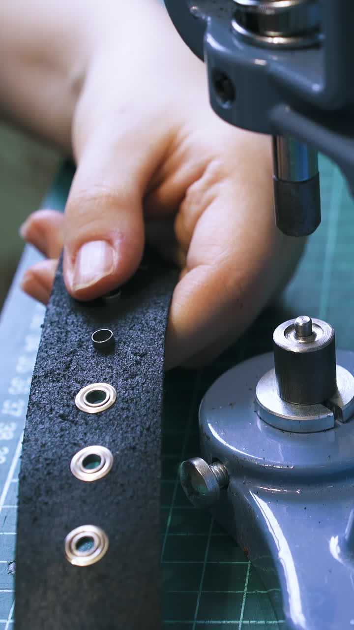 CU: Skilled girl tailor fixes eyelet parts in stylish black leather belt with press machine in workshop extreme close view