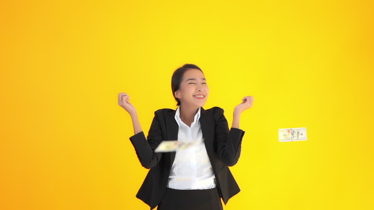 Slowmotion Asian woman office worker throws money in the air happily over yellow background