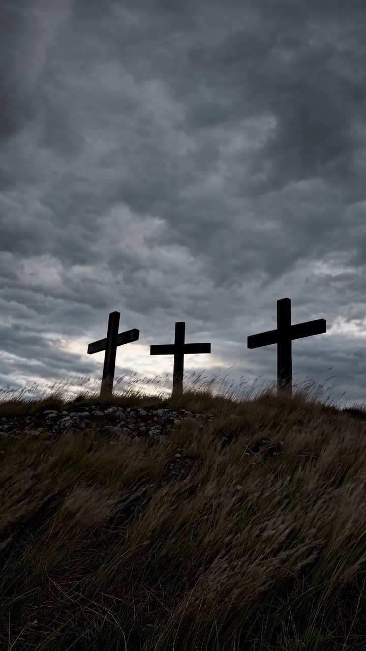 Dramatic video still of three crosses on a hill under a cloudy sky, captured from a low angle