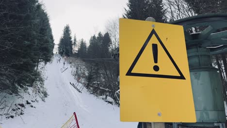 Large-warning-sign-on-ski-lift-indicates-danger-in-the-snow-on-the-ski-lift-going-up-the-slope-through-the-forest