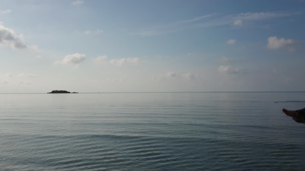 Woman in summer hat swinging on wooden swing over shallow and calm sea water at Karimun Jawa island with camera move to the left and beautiful blue sky background