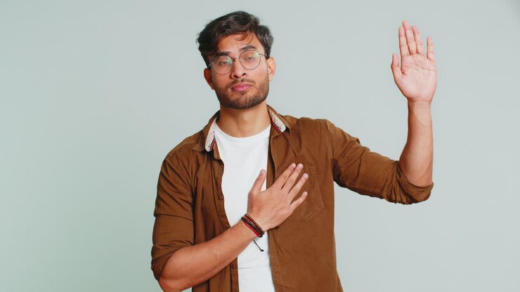 Uomo indiano che alza la mano per prestare giuramento, promettendo di essere onesto e di dire la verità, tenendo la mano sul petto.