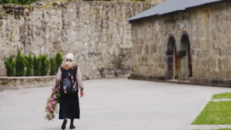 Old-Georgian-woman-carrying-flower-garland-to-stone-monastery-building