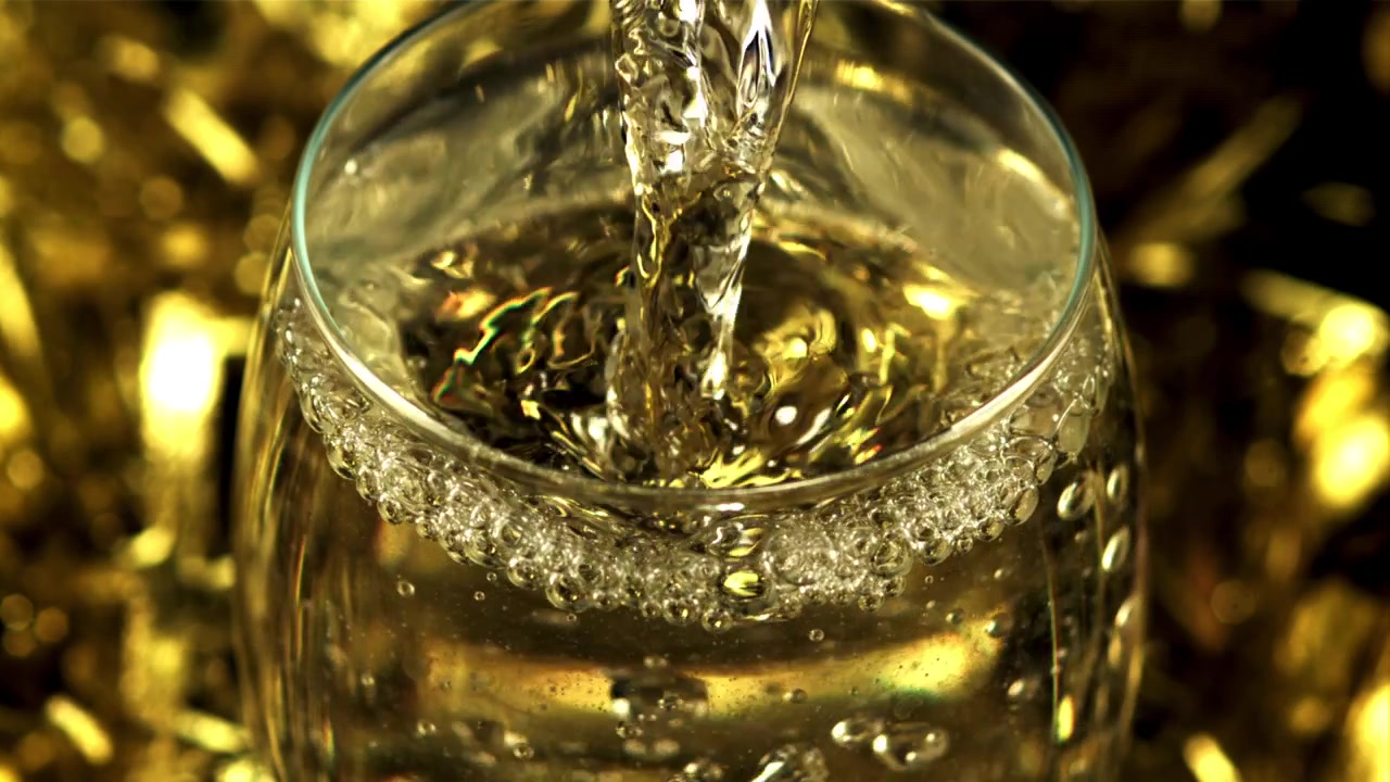 Versamento al rallentatore di vino bianco in un bicchiere con sfondo dorato