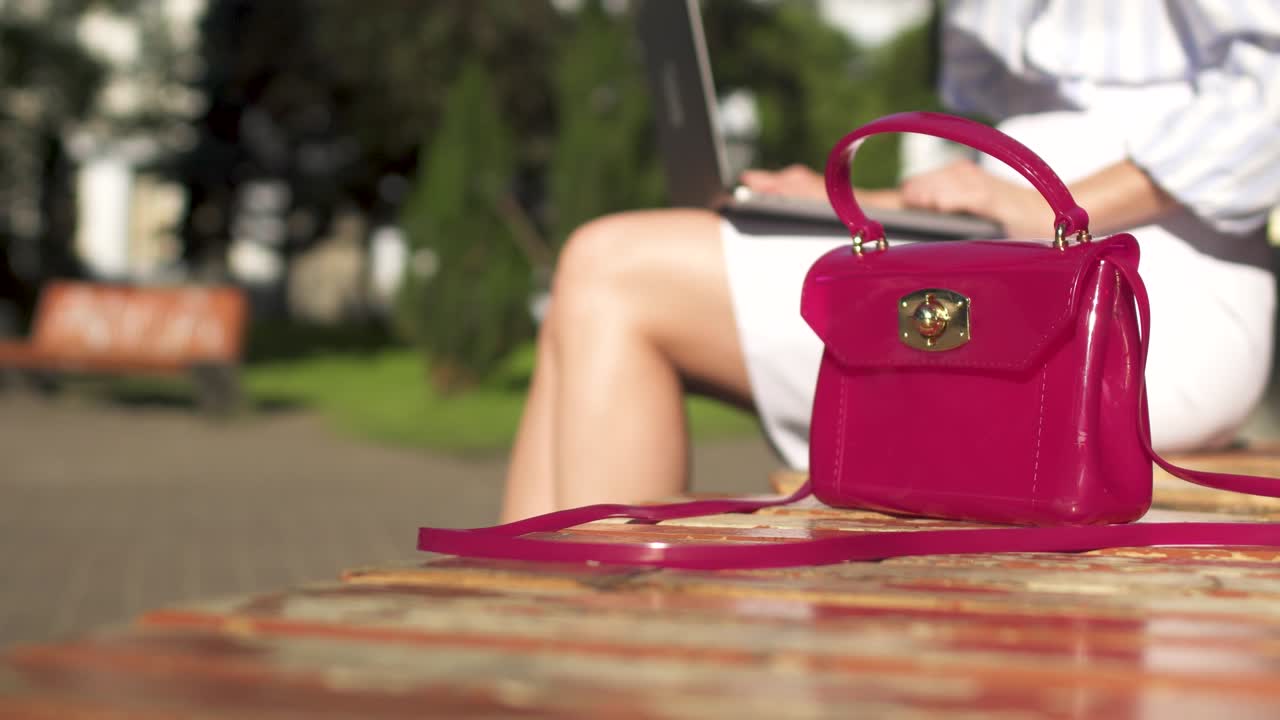 Woman close her laptop, take her pink bag from a bench in park and walk away