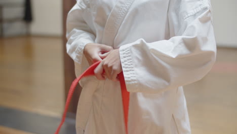 front view of woman tying orange belt on kimono in gym