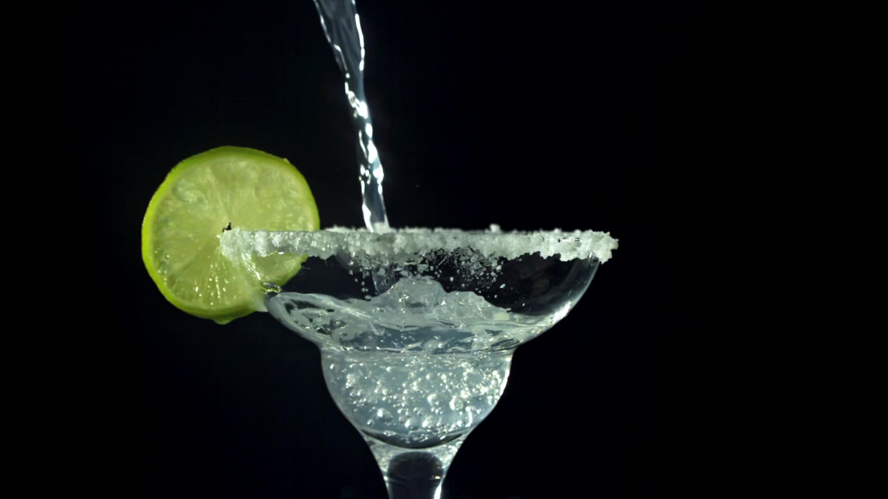 Versamento al rallentatore di un cocktail Margarita in un bicchiere bordato di sale con lime