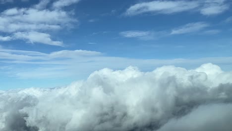 Flying-over-some-fluffy-cumulus-clouds-with-a-deep-blue-sky,-shot-from-a-jet-cockpit