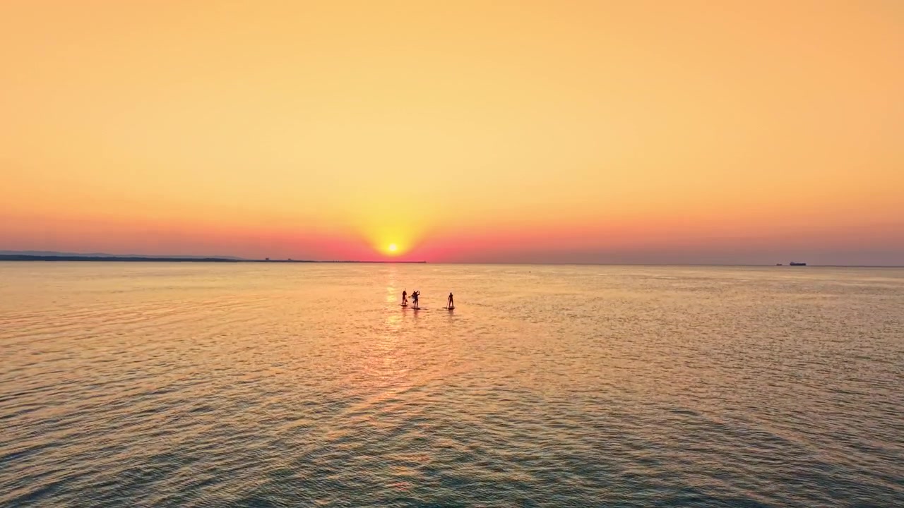 People enjoy the sunset by the water while standing in the waves as the sun sets on the horizon during evening hours