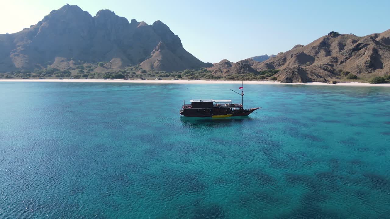 Endonezya'nın Komodo Adası'nın el değmemiş sahil şeridinin önünde turistik teknenin havadan görünümü.