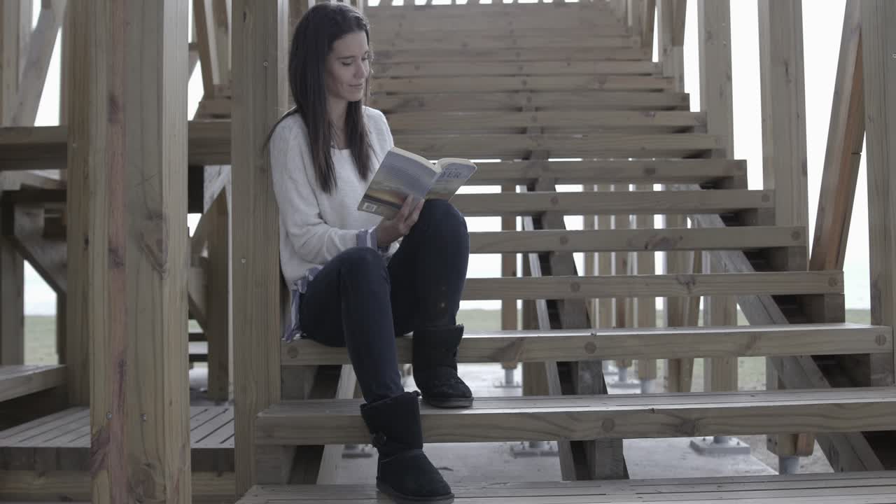 Giovane donna che legge un libro seduta su gradini di legno