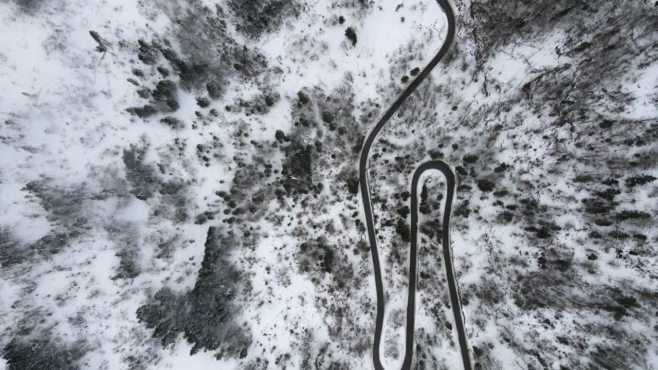 Aerial dolly directly above mountain road car winter snow pine trees mist day