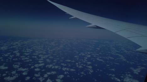 una toma acercándose a la ventana de un avión comercial y mostrando el ala y miles de pequeñas nubes