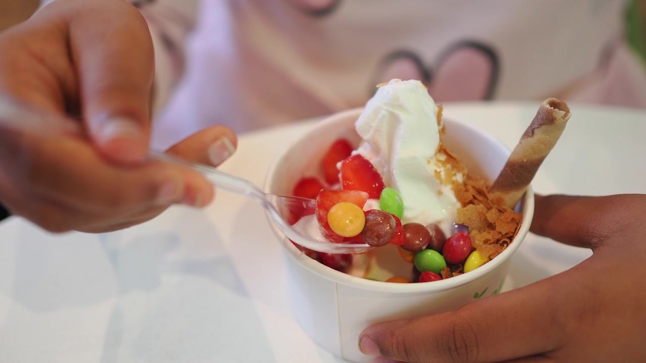 Persona che mangia yogurt gelato con guarnizioni da una coppetta di carta