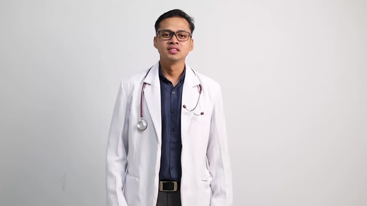 Dokter Asia bahagia dengan jas medis putih menari di atas latar belakang studio putih