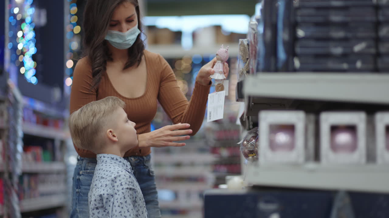 una madre enmascarada elige juguetes navideños con su hijo antes de navidad