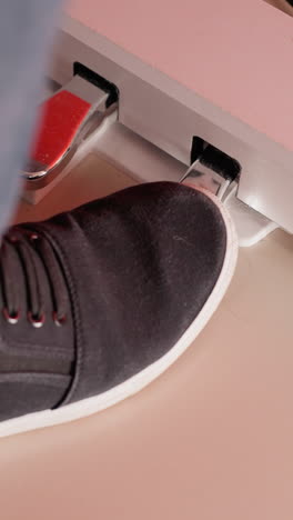 a foot wearing a black shoe and blue jeans gently tapping on a piano pedal. the scene is highlighted by a soft red hue in the background, adding warmth and depth