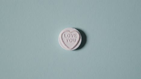 Hand-Picking-Up-Heart-Candy-With-Love-You-Message-On-Blue-Background