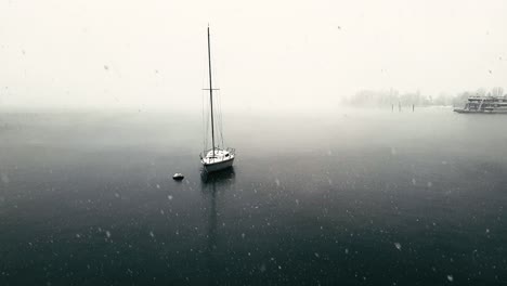 surreal scene of snow falling over maggiore lake and moored sailing boat and ferryboats, italy