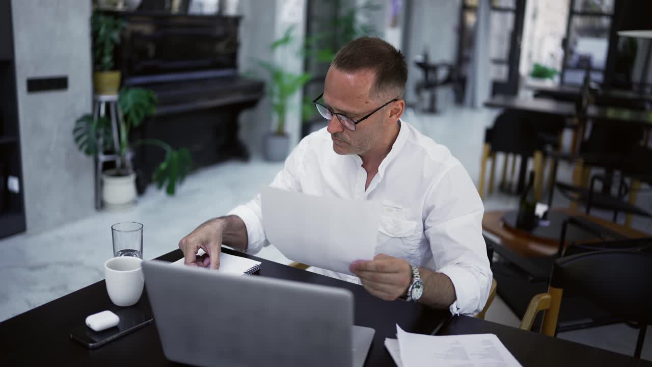 Focused adult businessman working on project, writing paper notes, sitting at cafe desk. Concentrated male professional