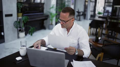 hombre de negocios adulto concentrado trabajando en un proyecto, escribiendo notas en papel, sentado en el escritorio de un café. concentrado profesional masculino