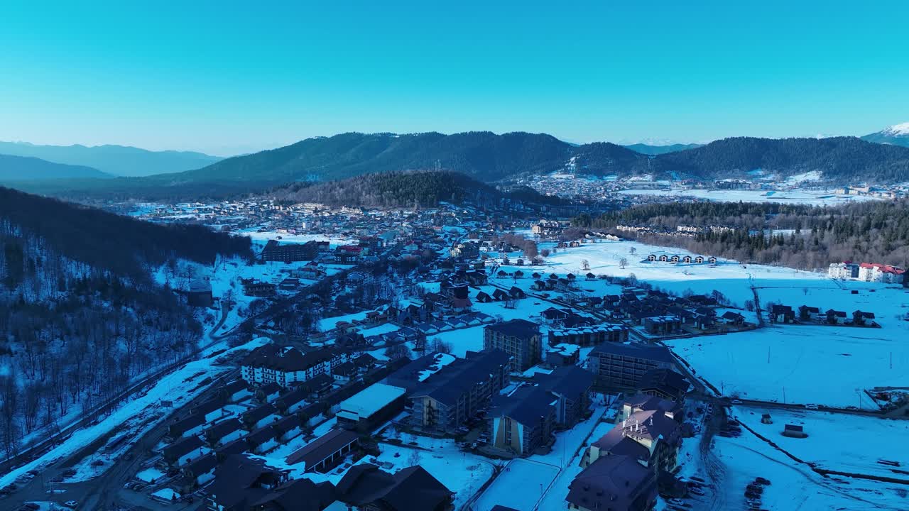 A breathtaking aerial view of a dense forest blanketed in snow, with majestic snow-capped mountains in the background, capturing the pristine beauty of winter