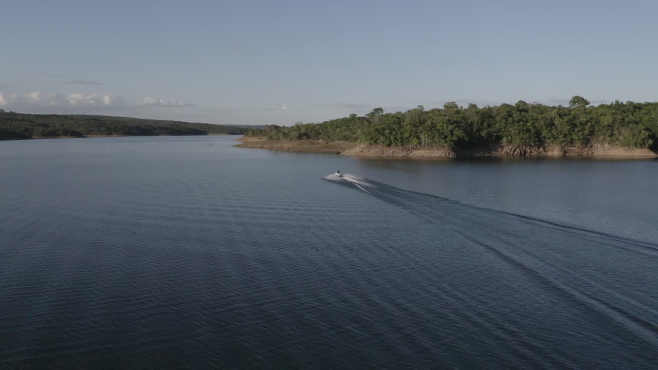 persona en una moto de agua a toda velocidad a lo largo de un gran lago idílico a lo largo de la costa tropical - vista aérea