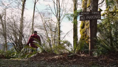 hombre caminando en un bosque lluvioso de la costa oeste en la isla de vancouver canadá con un cartel de sendero de playa en un árbol que conduce a la playa