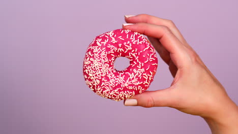 pink donut with sprinkles held in a hand
