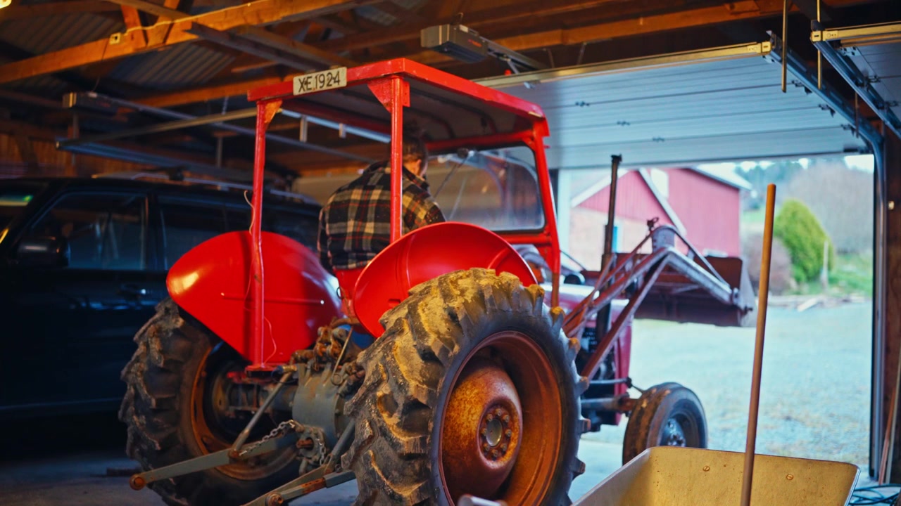 A Red Tractor is Driving Out of the Garage, Moving Forward Into the Open Rural Area - Static Shot