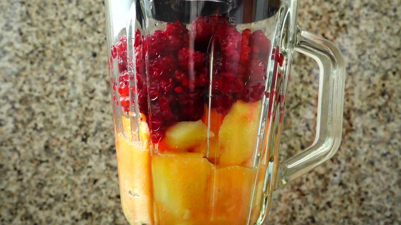 Preparazione di un cocktail nel frullatore con mele, banane e lamponi. Movimento rallentato.