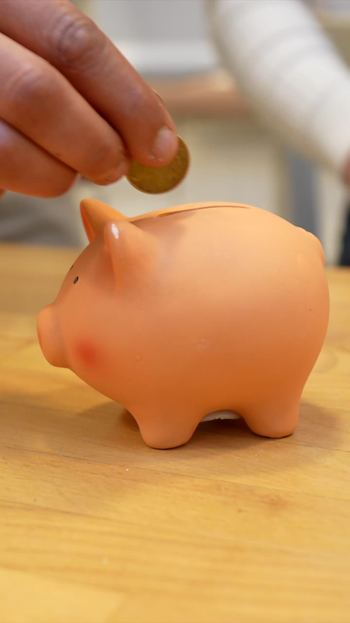 Hand Putting Coins into a Pink Piggy Bank on a Wooden Table