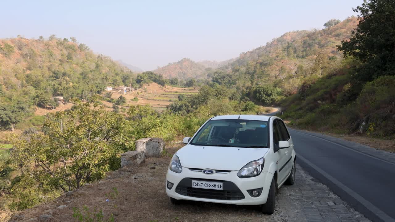 White car parked on a scenic mountain road with hills in the background