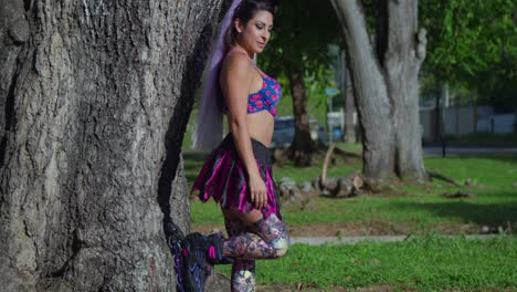 Left-pan-of-a-young-woman-in-roller-blades-at-the-park-leans-on-a-tree-trunk