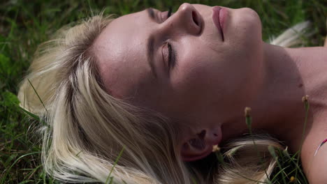 a young blonde girl lies on the green grass with her eyes closed and is dreaming or sleeping